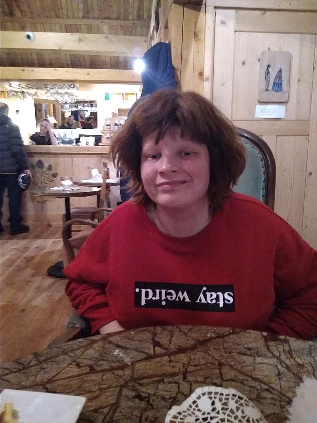 Justyna siedzi przy stoliku w restauracji. Ma bluzę z odwróconym do góry nogami napisem: stay weird