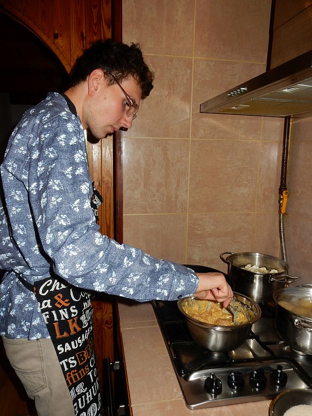 Tomasz przy kuchence miesza coś w garnku