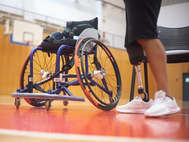 na sali gimnastycznej wózek inwalidziki obok widać nogi mężczyzny, jedna to proteza