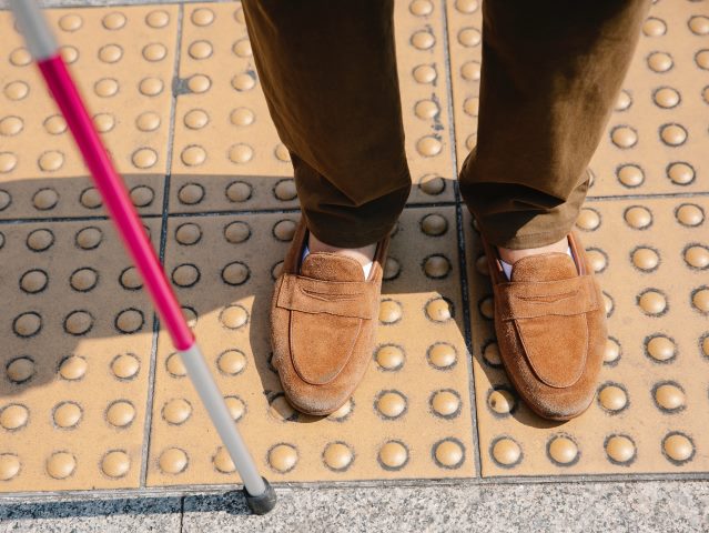 męskie nogi stoją na guzikach na chodniku obok biała laska