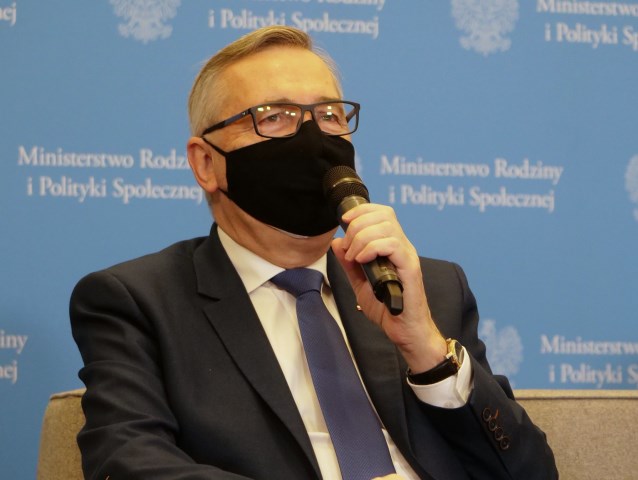 Stanisław Szwed w maseczce siedząc mówi do mikrofonu