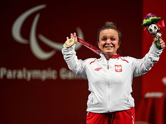 Uradowana Justyna Kozdryk trzyma medal jedną ręką, a w drugiej ma maskotkę igrzysk