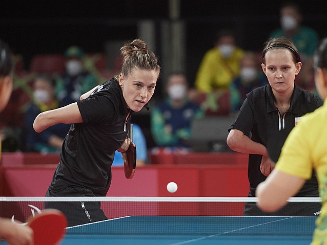 Natalia Partyka i Karolina Pęk przy stole tenisowym podczas meczu. Partyka właśnie zaserwowała piłeczkę