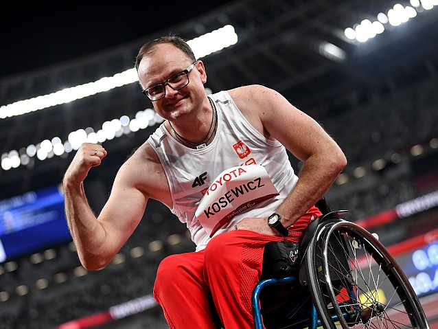 Piotr Kosewicz w stroju reprezentanta Polski, siedzi na wózku prężąc muskuły