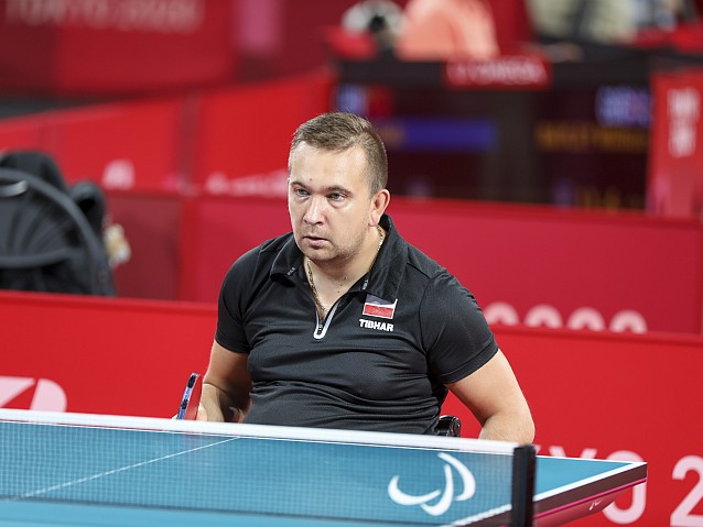 Rafał Czuper siedzi na wózku przy stole tenisowym z rakietką w ręku