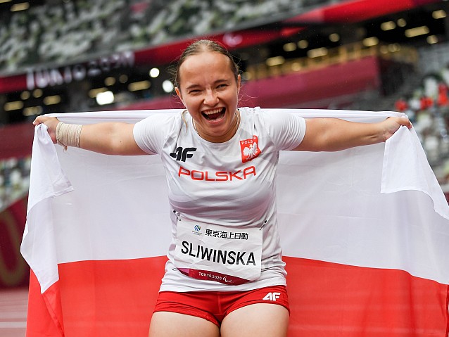 Renata Śliwińska na stadionie lekkoatletycznym. Krzyczy z radości trzymając za sobą rozpostartą polską flagę
