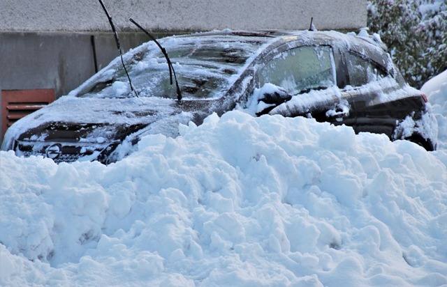Samochód zasypany śniegiem na parkingu zimową porą, auto przykryte białym puchem śnieżnym