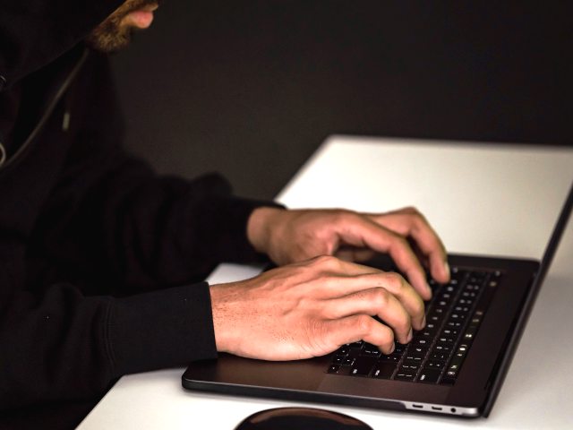 mężczyzna w kapturze pisze na klawiaturze komputera