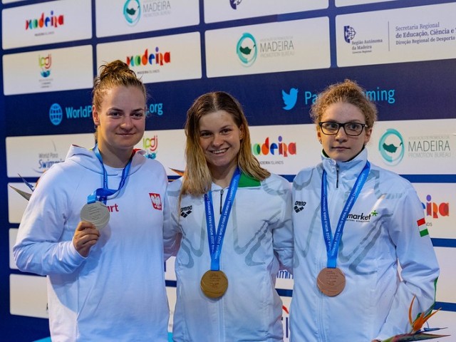 Trzy zawodniczki z medalami na podium, w tym Oliwia Jabłońska trzyma w dłoni srebrny medal