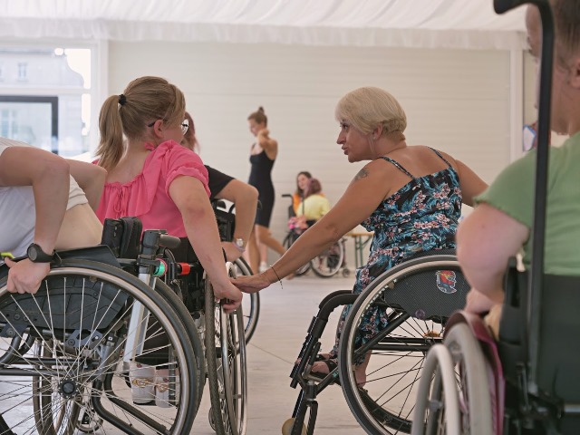 Uczestniczka na wózku i trenerka na wózku podczas zajęć tanecznych.