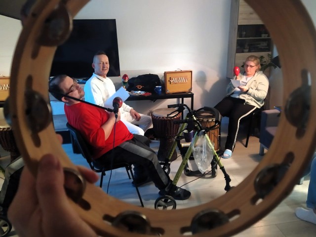 Zdjęcie przedstawia dwóch mężczyzn oraz kobietę z instrumentami muzycznymi podczas zajęć.