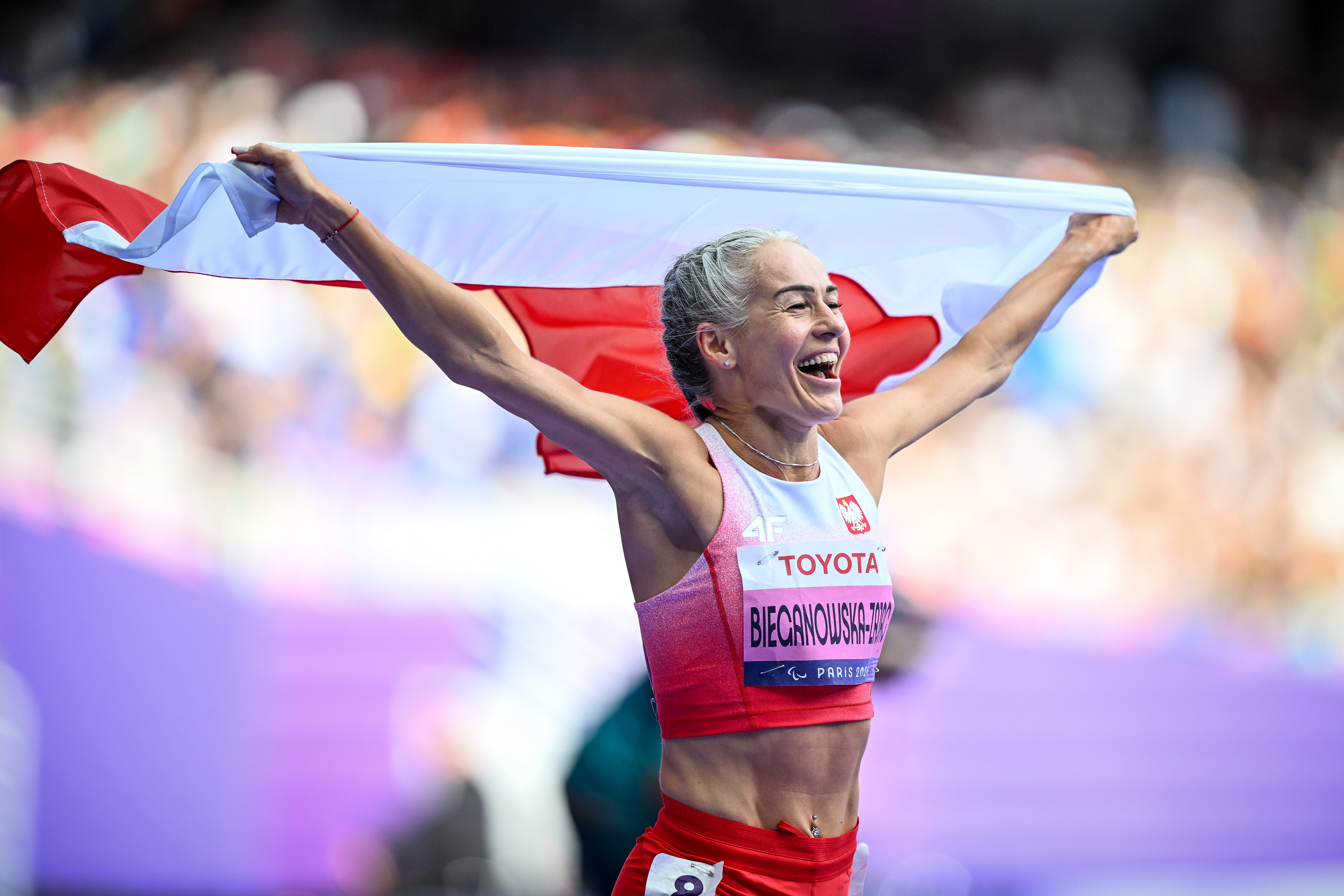 Biegaczka Barbara Bieganowskaunosi w geście tryumfu polską flagę nad głową.