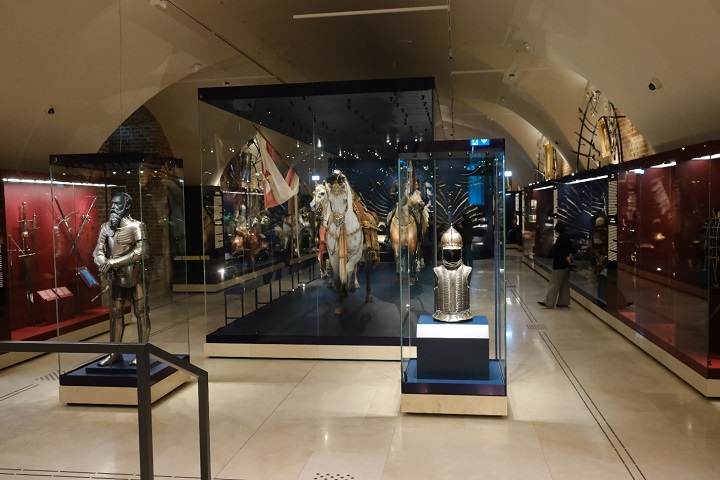 Na zdjęciu przedstawione są eksponaty muzealne, miecze, rzeźby w gablotach.