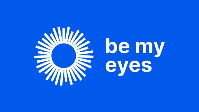 Białe logo aplikacji "Be my eyes" w formie geometrycznego słońca na jaskrawo niebieskim tle.