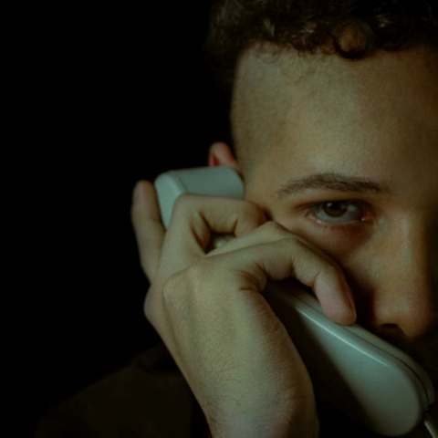 Twarz młodego mężczyzny, zasłonięta telefonem, trzymanego przy uchu.  