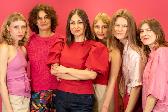 Na zdjęciu na różowym tle znajduje się sześć kobiet. Ubrane na różowo przedstwicielki Fundacji Różowa Skrzyneczka.
