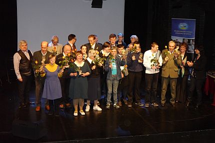 Aktorzy i organizatorzy Teatru Ubogiego Relacji stoją na scenie ze statuetkami i z kwiatami