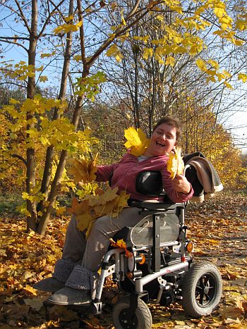 Roześmiana kobieta na wózku elektrycznym wśród pożółkłych liści