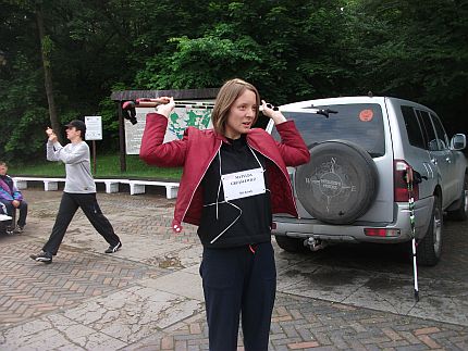 Młoda kobieta stoi w parku z kijkami do nordic walkingu trzymanymi za głową
