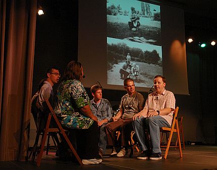 Aktorzy Grupy Od Nowa siedzą na scenie na krzesłach, w tle wyświetlane czarno-białe zdjęcia