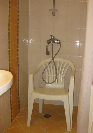 Prysznic w hotelowym pokoju z plastikowym krzesełkiem stojącym na środku