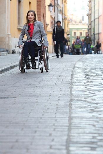 Kobieta na wózku jedzie wózkopasem na warszawskiej Starówce