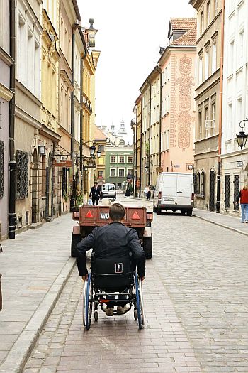 Mężczyzna na wózku jedzie wózkopasem, który jest jednak zastawiony samochodową przyczepką